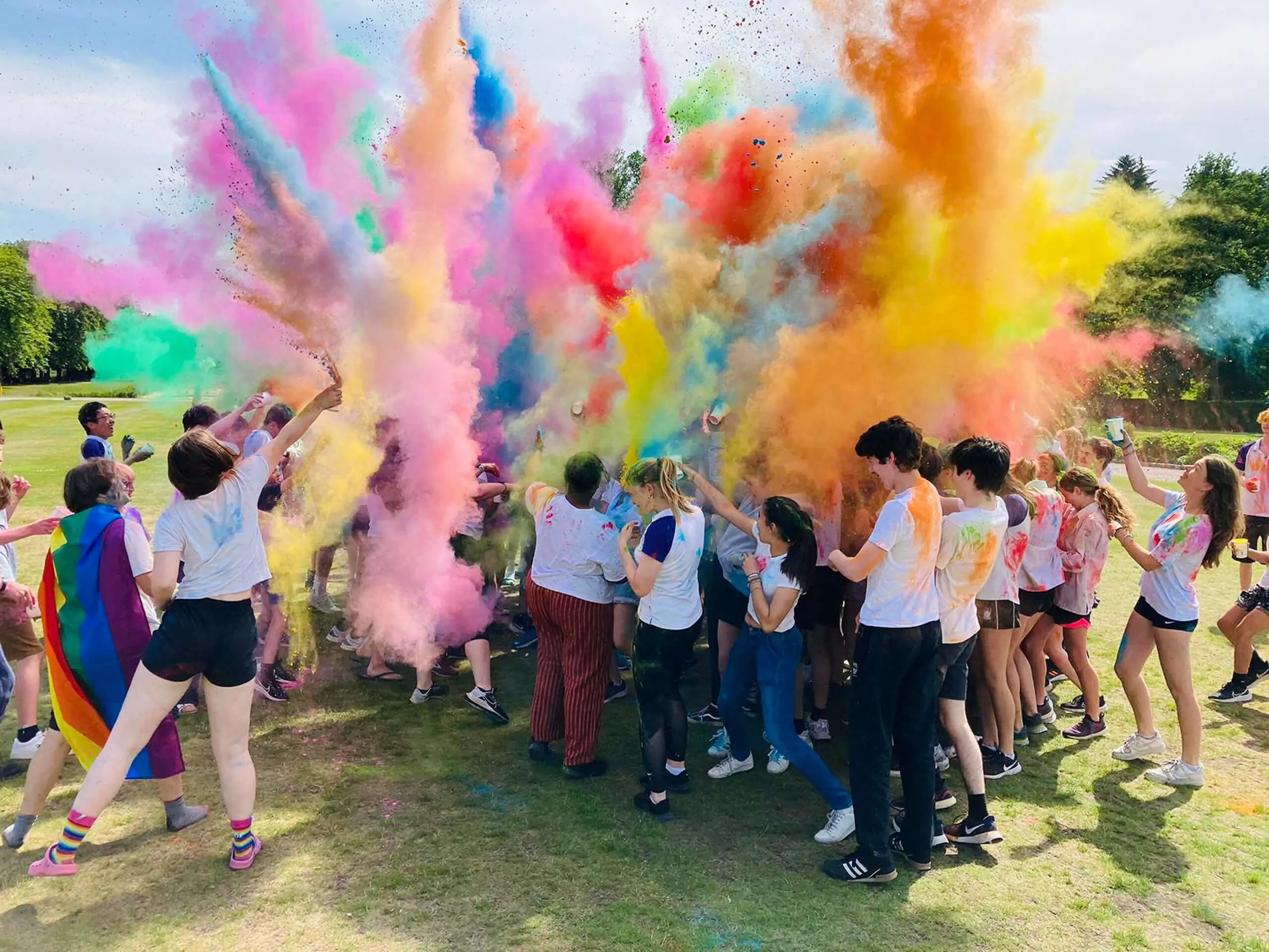 Students celebrating at an outdoor event with bright colored powder thrown in the air.