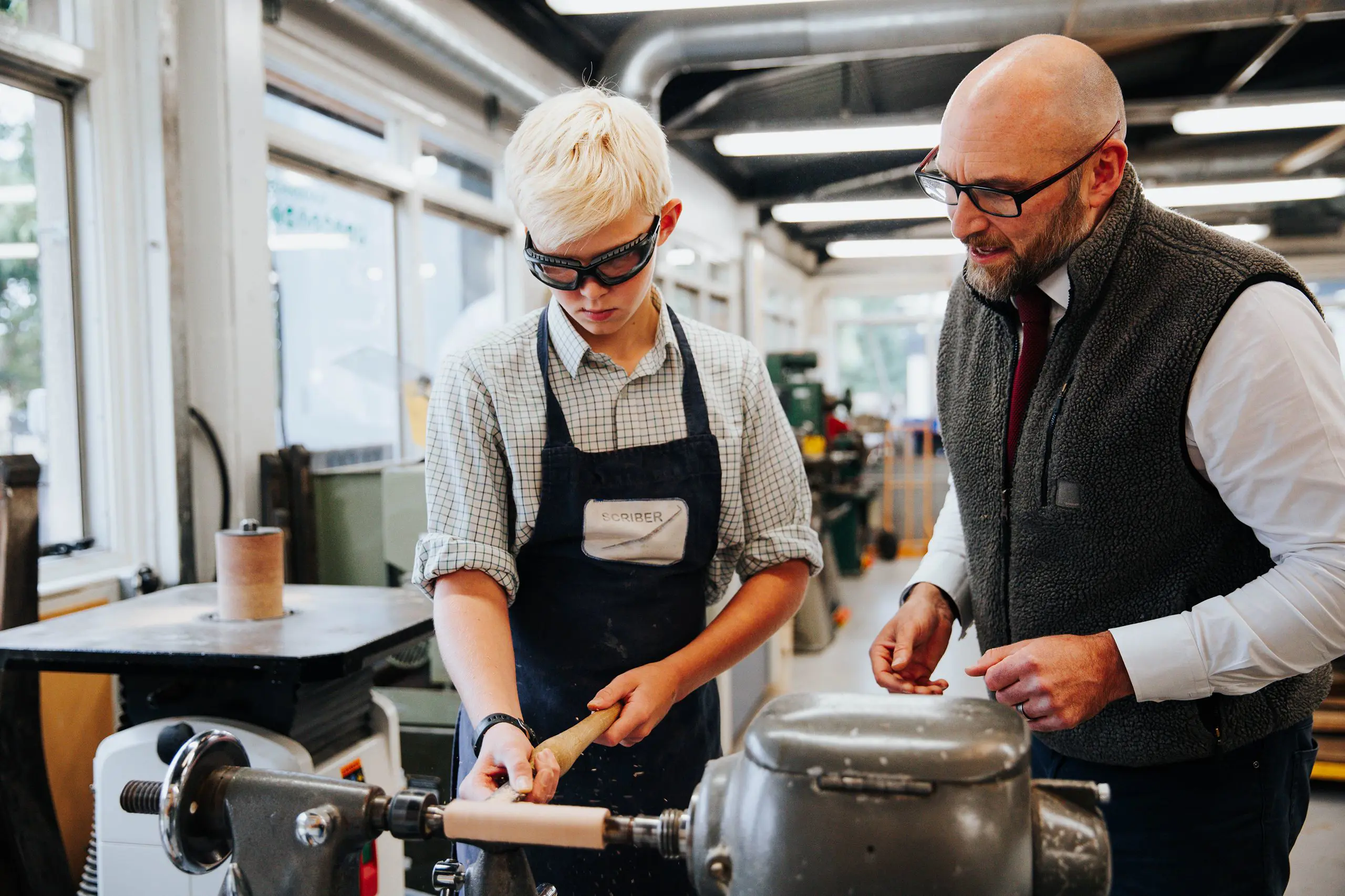 Teacher guiding a student while working with a wood lathe machine in a modern design technology workshop.