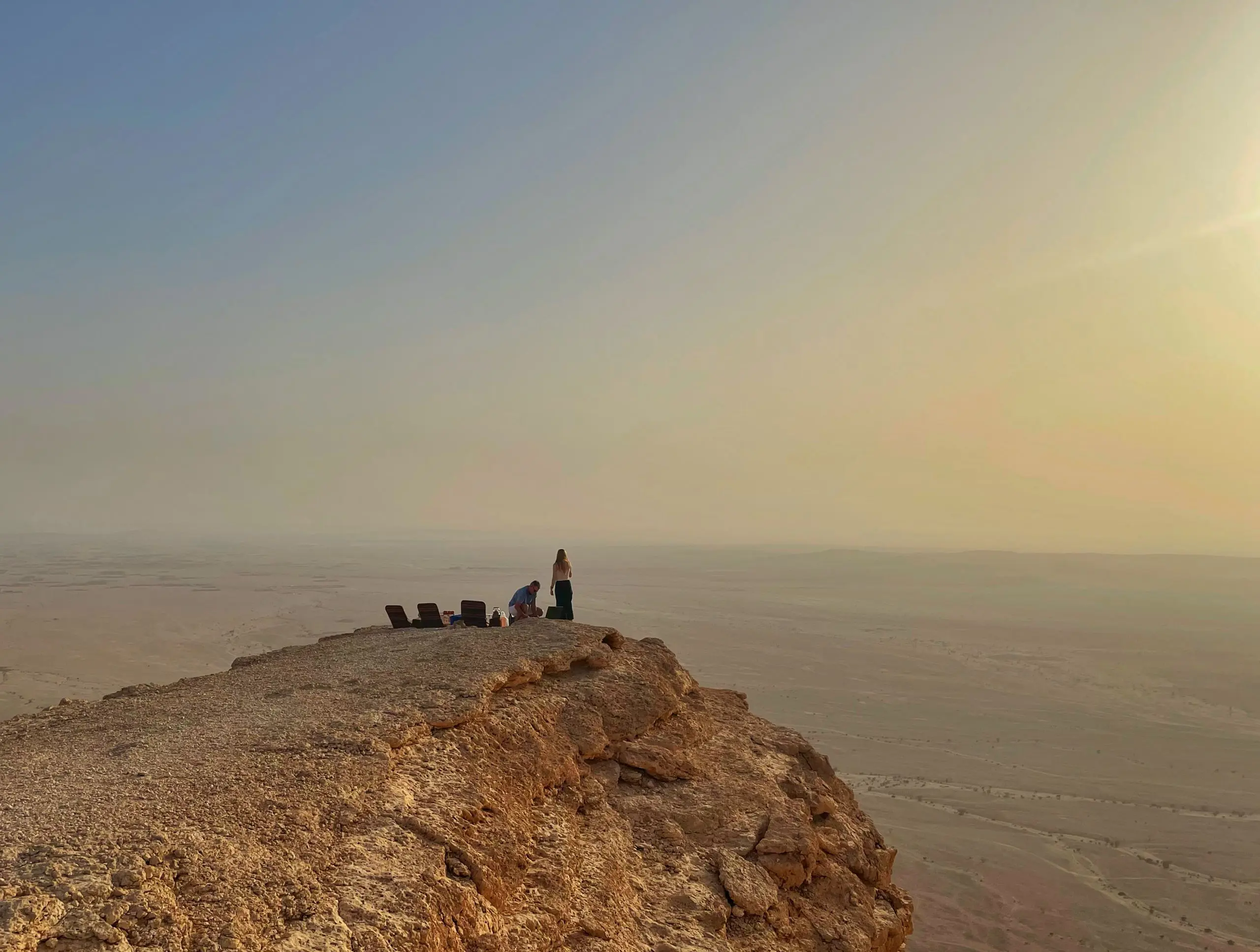 Group of students silhouetted on a rocky cliff edge overlooking a scenic landscape.