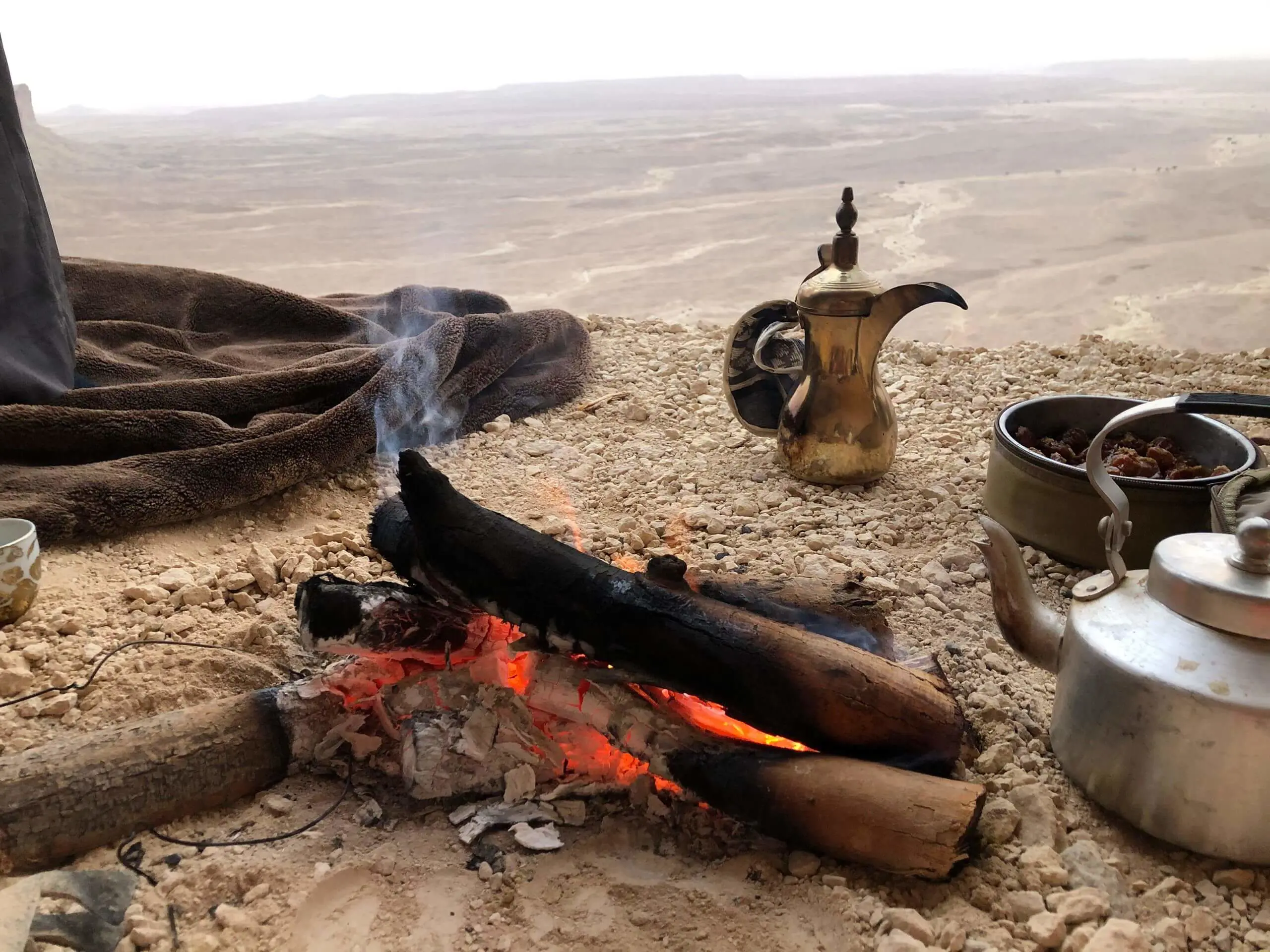 Traditional Arabic dallah coffee pot resting over a glowing campfire outdoors.