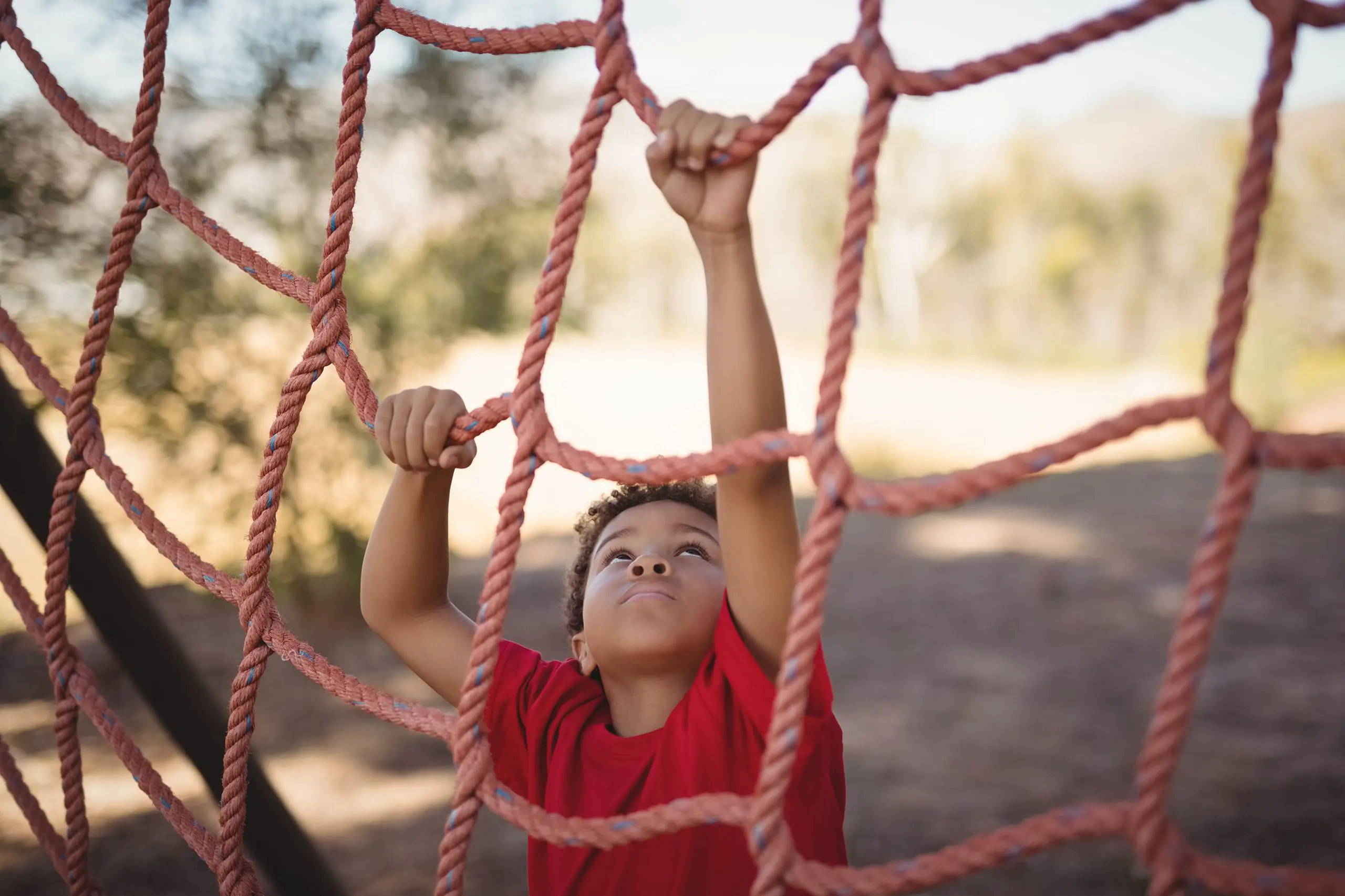 Young student climbing up a outdoor rope net climbing structure.