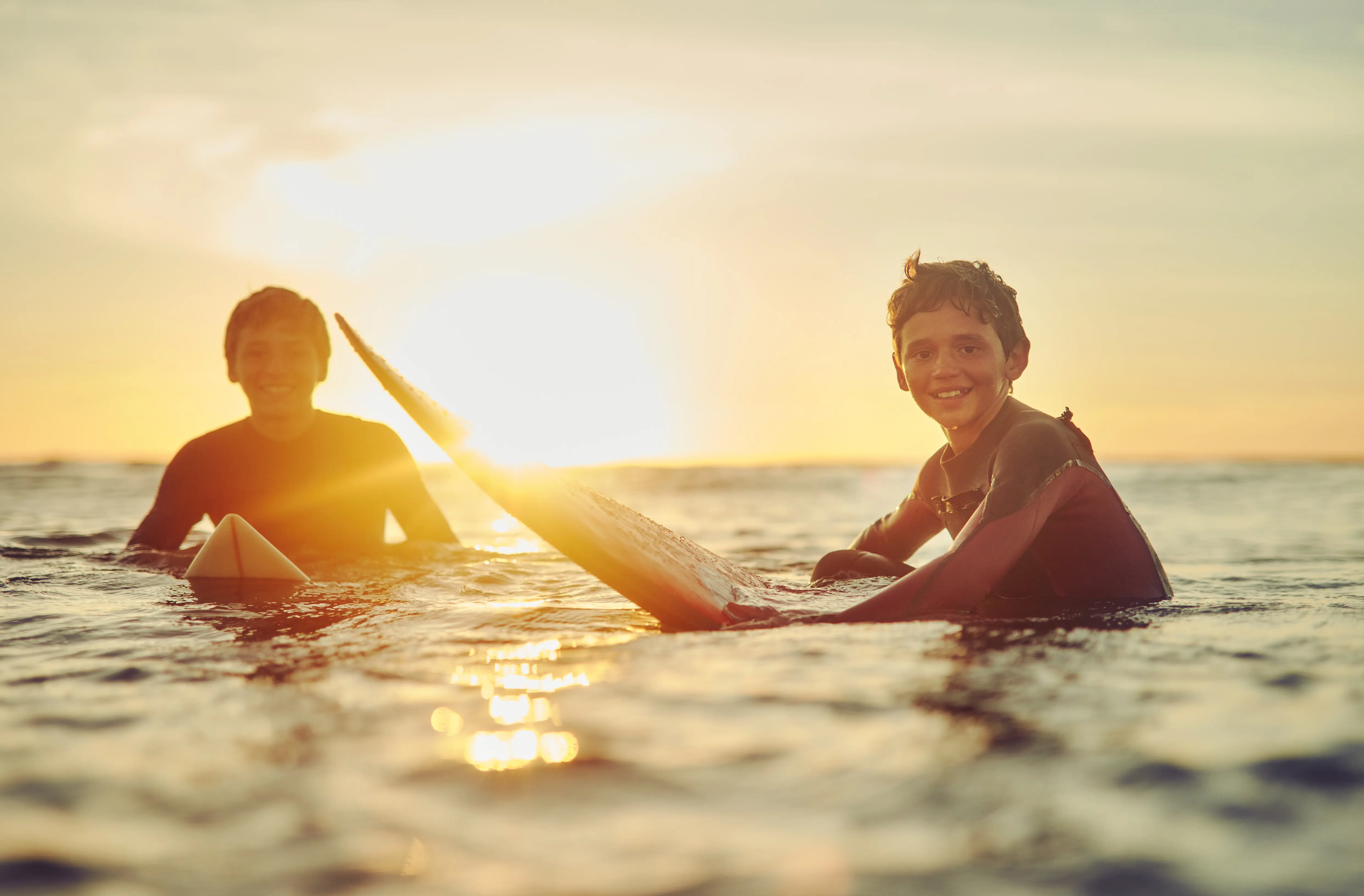 Two young students smiling during a water sports activity at sunset on the water.