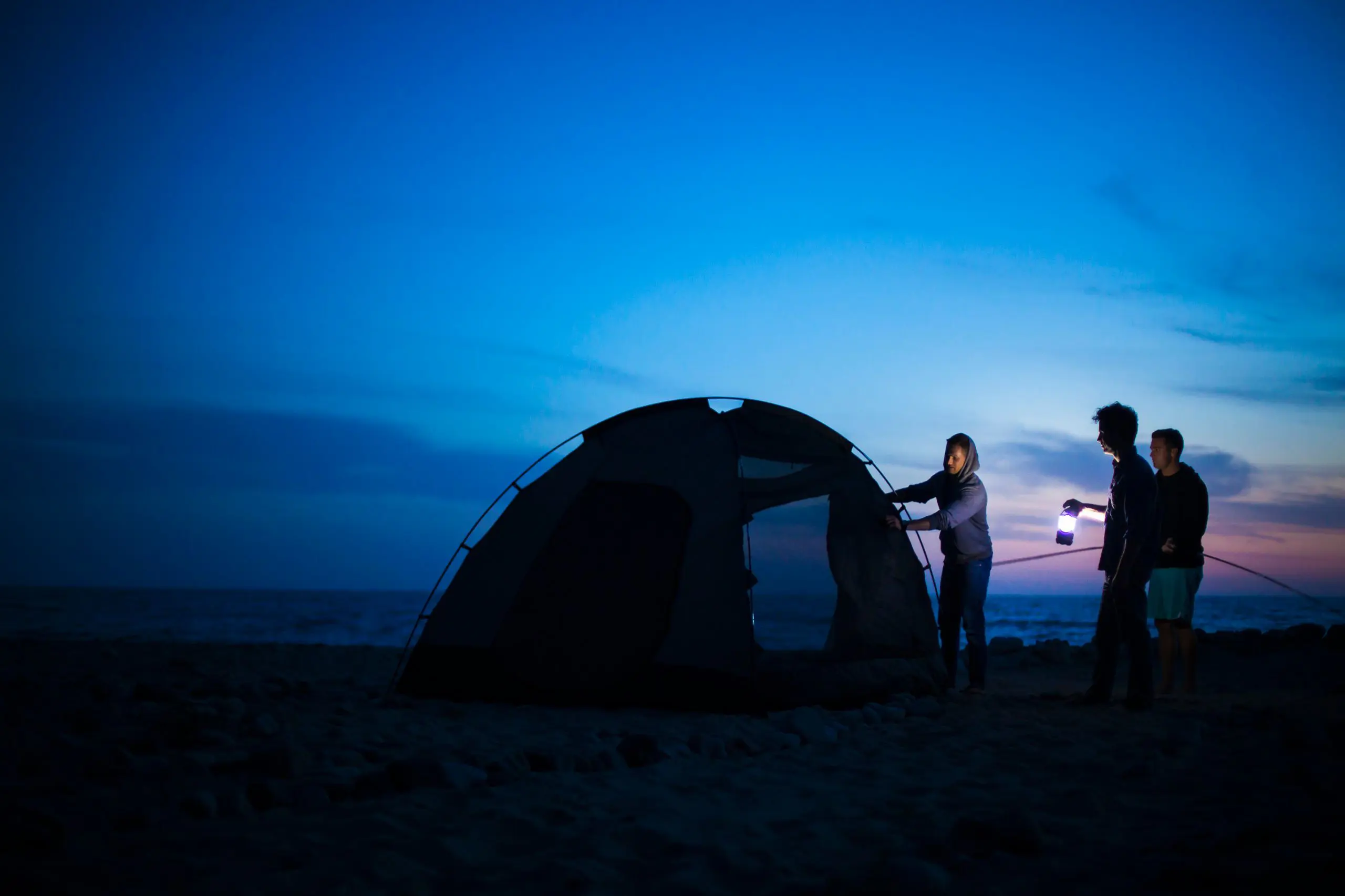 Person sitting outside a camping tent set up under a dark starry sky.
