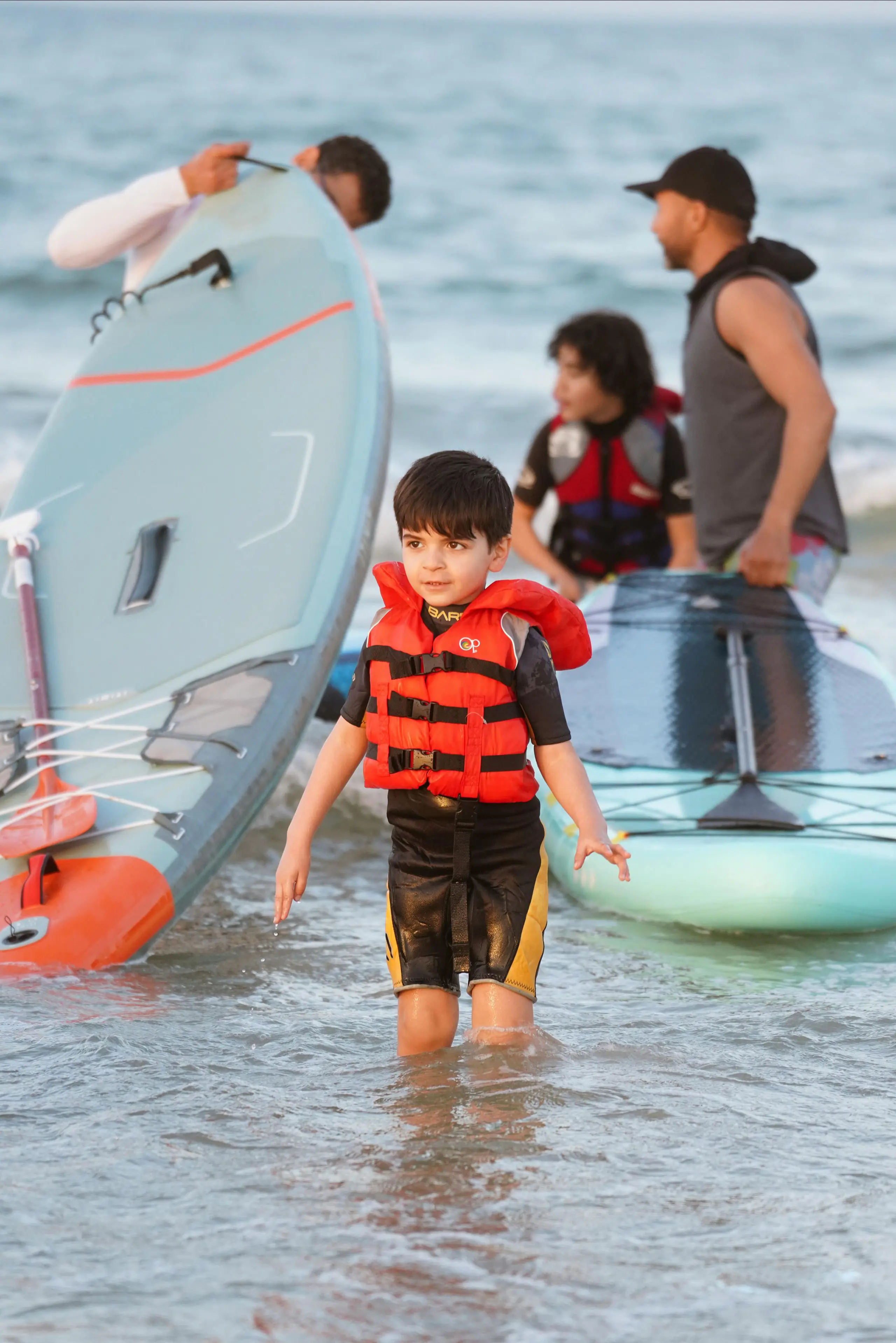 Young students wearing safety life jackets carrying paddleboards towards the shore.