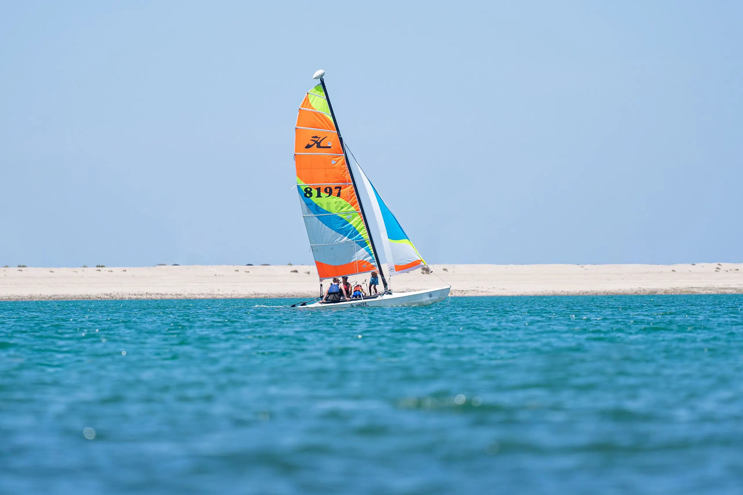 Small sailboat with a vibrant, colorful sail gliding across calm turquoise water
