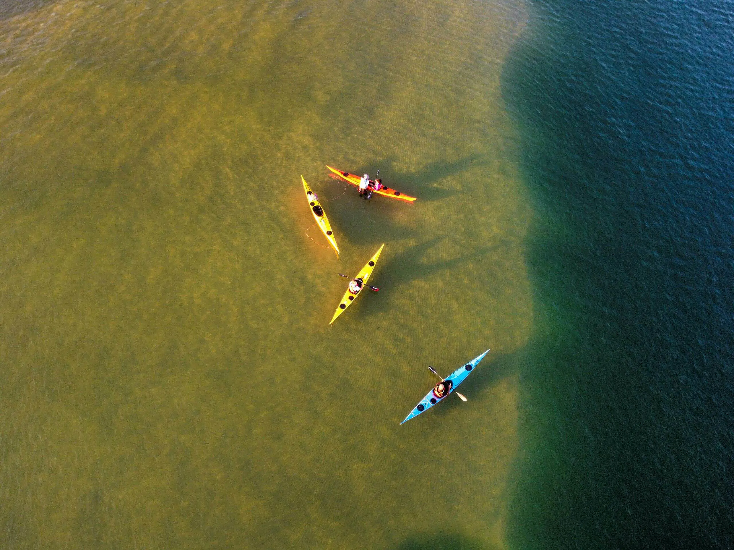 Aerial view of students paddling yellow kayaks through clear turquoise coastal waters.